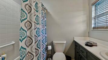 A bathroom with a patterned shower curtain, a toilet, a sink, and a window with blinds.
