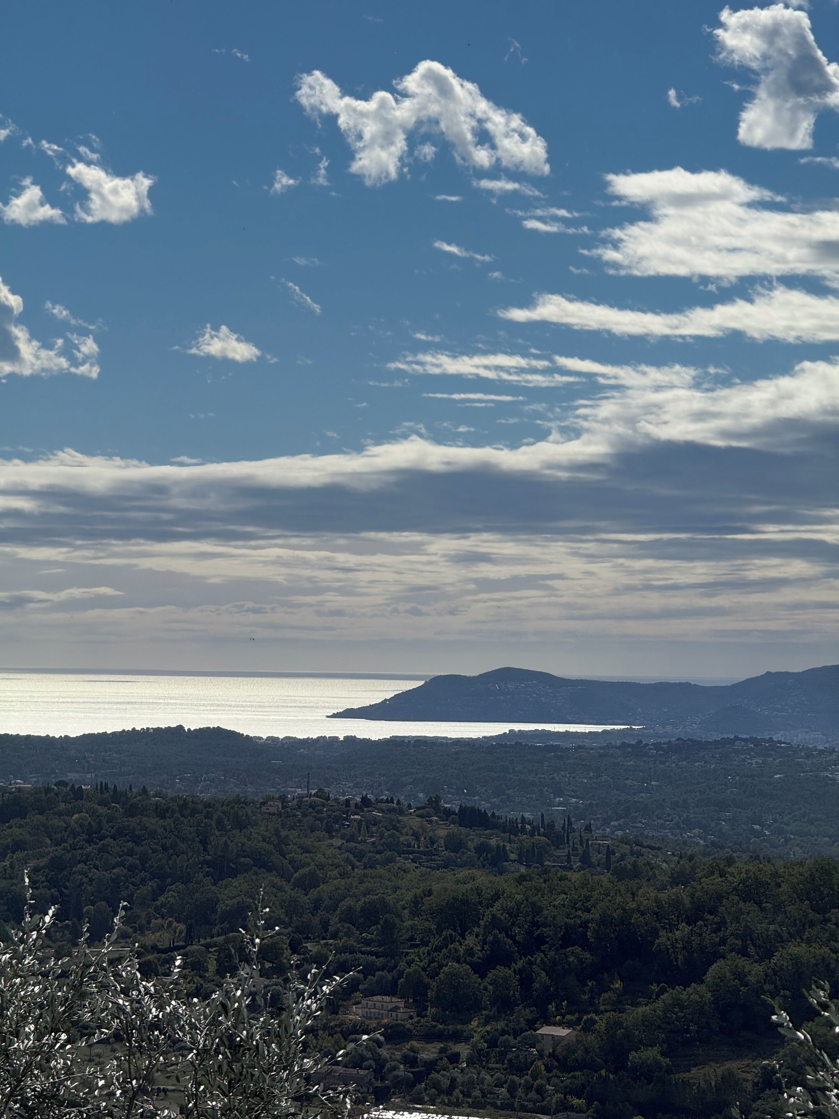 A coastal landscape with a view of the sea, hills, and a city in the distance.