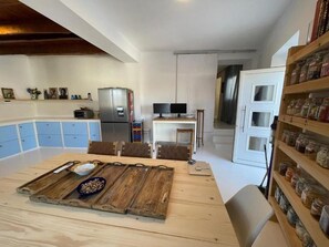 Eine moderne Küche mit einem Holztisch, Stühlen, einem Kühlschrank, einer Mikrowelle und einem Fernseher. Es gibt Schränke und eine Ablage mit Gläsern.