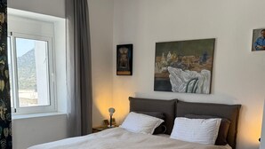 Ett välordnat sovrum med en stor säng, ett sängbord, en lampa och ett fönster med gardiner.