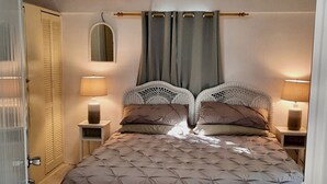 Ein Schlafzimmer mit einem Bett, zwei Nachttischen mit Lampen, einem Spiegel und einem Fenster mit Vorhängen.
