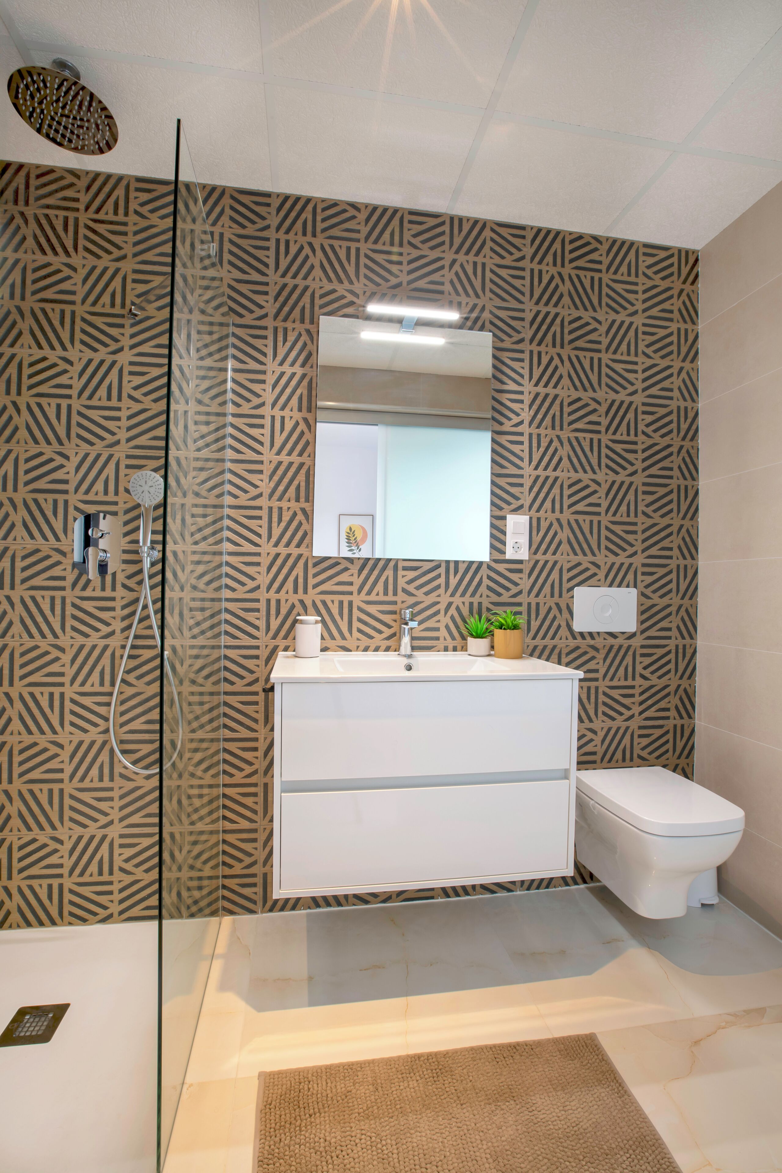 Une salle de bain moderne avec un papier peint à motifs, un meuble-lavabo blanc, des toilettes et une douche à parois de verre.