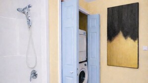 A bathroom with a bathtub, a washing machine, and a door leading to another room.