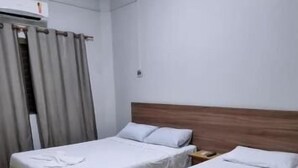 Et hotelværelse med to enkeltsenge, en træsengegavl, et lille træbord og et vindue med gardiner.