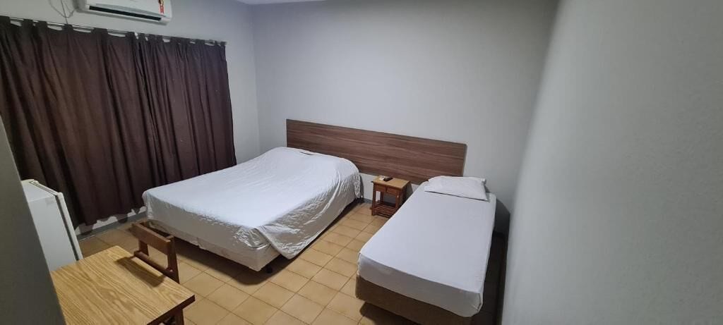 Habitación de hotel con dos camas, una mesita de noche de madera, una pequeña mesa y una ventana con cortinas.