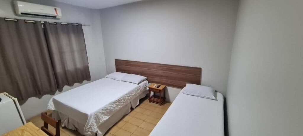 Hotellihuone, jossa on kaksi sänkyä, puinen pääty, yöpöytä ja pieni pöytä.