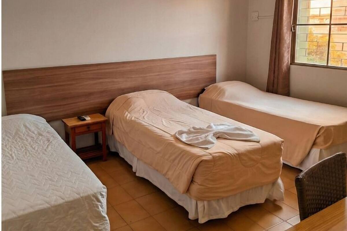 Una habitación de hotel con dos camas individuales, una mesita y un ventanal con cortinas.