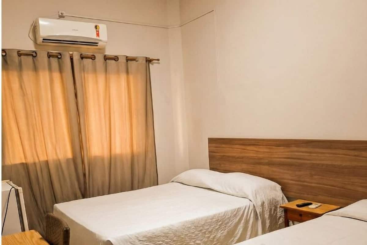 Habitación de hotel con dos camas, un escritorio de madera, una silla, un equipo de aire acondicionado y una cortina.