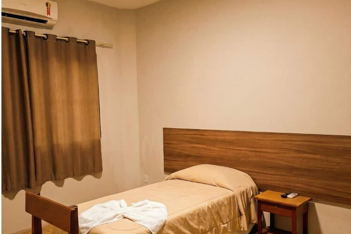 Una habitación pequeña con una cama individual, cabecera de madera, mesita de noche y ventana con cortinas.