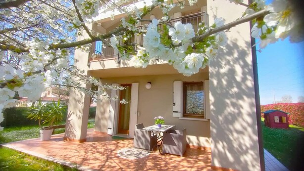 A two-story building with a balcony, a dining area with a table and chairs, and a small garden area with a potted plant. - VILLA VENEZIA (Mira)