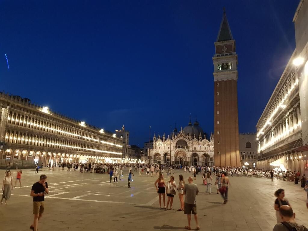 A spacious square with historic buildings, a prominent clock tower, and a large open area for gatherings.
