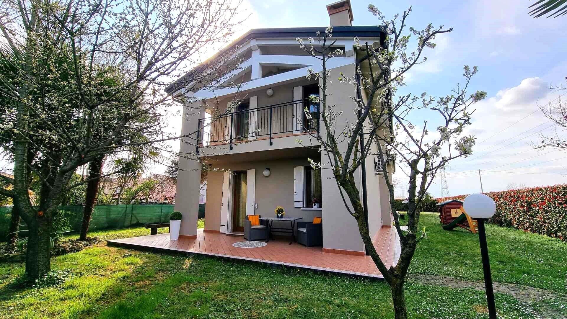 A two-story house with a balcony, a patio with outdoor furniture, and a well-maintained garden.