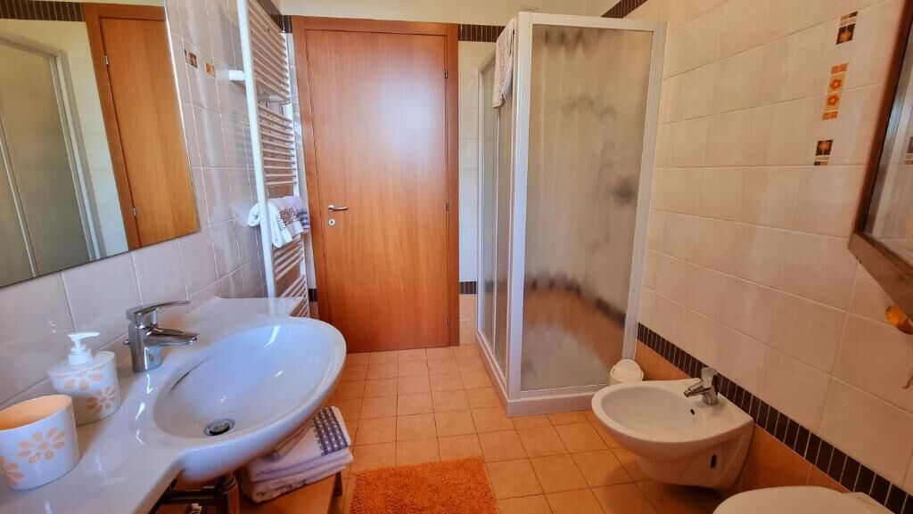 A bathroom with a sink, bidet, shower, and a wooden door.