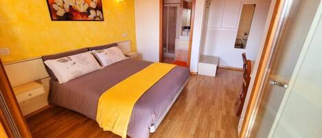 A bedroom with a bed, wooden flooring, a painting on the wall, and a door leading to a bathroom.