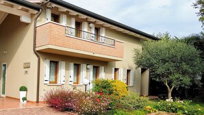A two-story house with a balcony, a patio with outdoor furniture, and a garden with various plants and flowers. - VILLA VENEZIA (Mira)