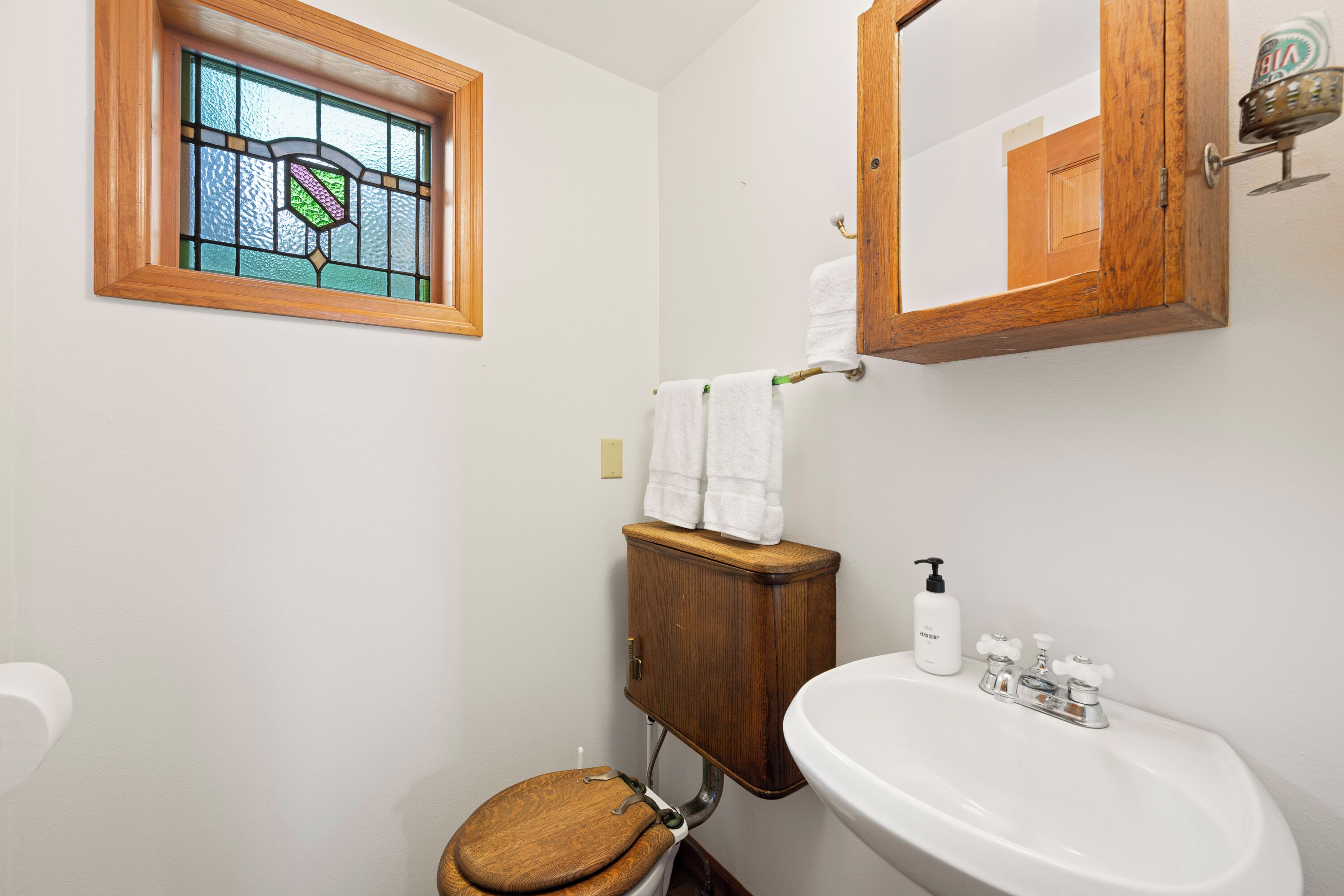 A bathroom with a wooden toilet, a white sink, a mirror, and a stained glass window.