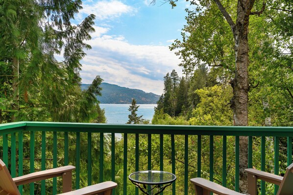 A deck with a table and chairs overlooking a lake with trees and mountains in the background. - Waterfront Retreat with Private Dock & Lake Views (Sandpoint)