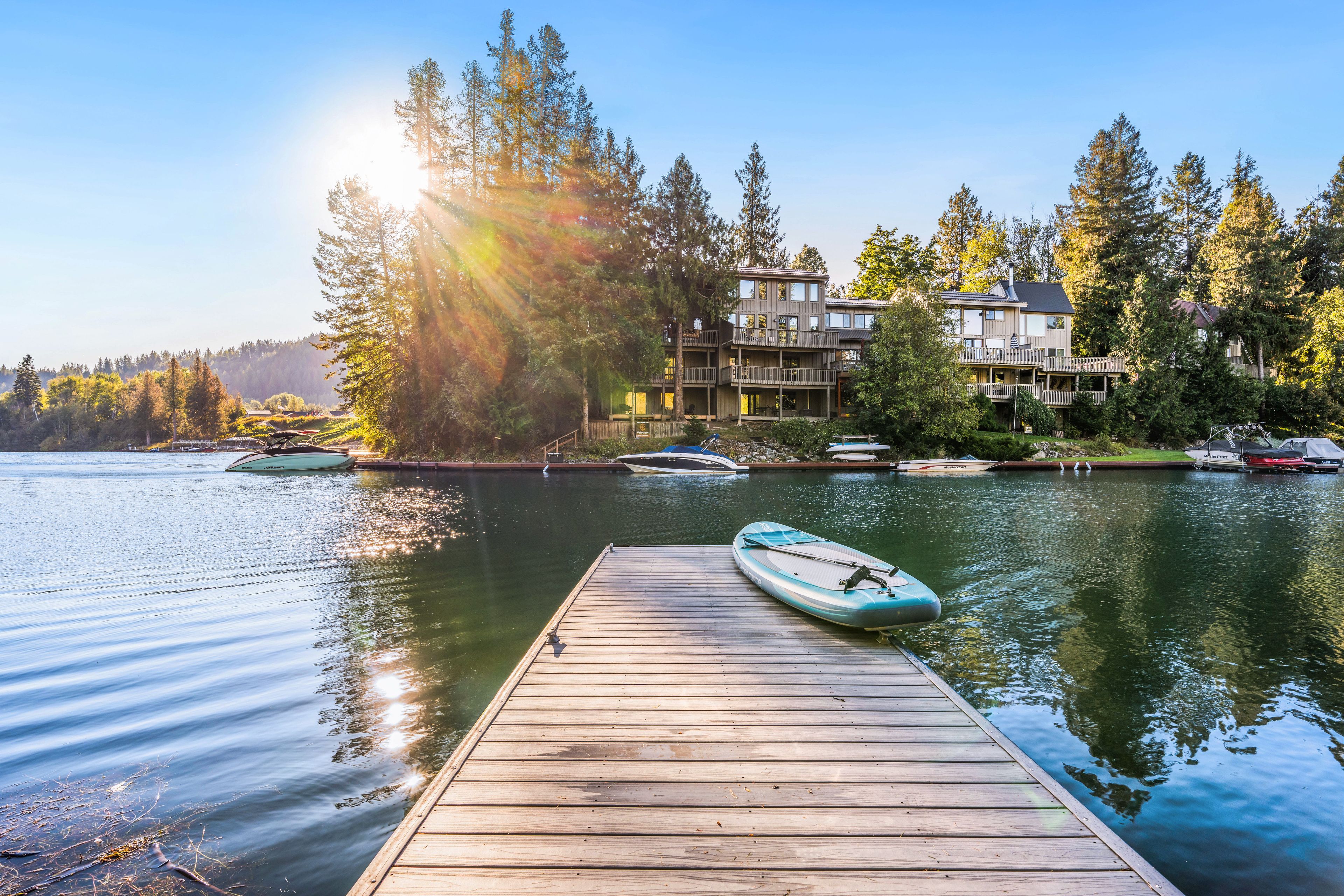 A wooden dock leading to a calm lake with boats, surrounded by multi-story buildings with balconies.