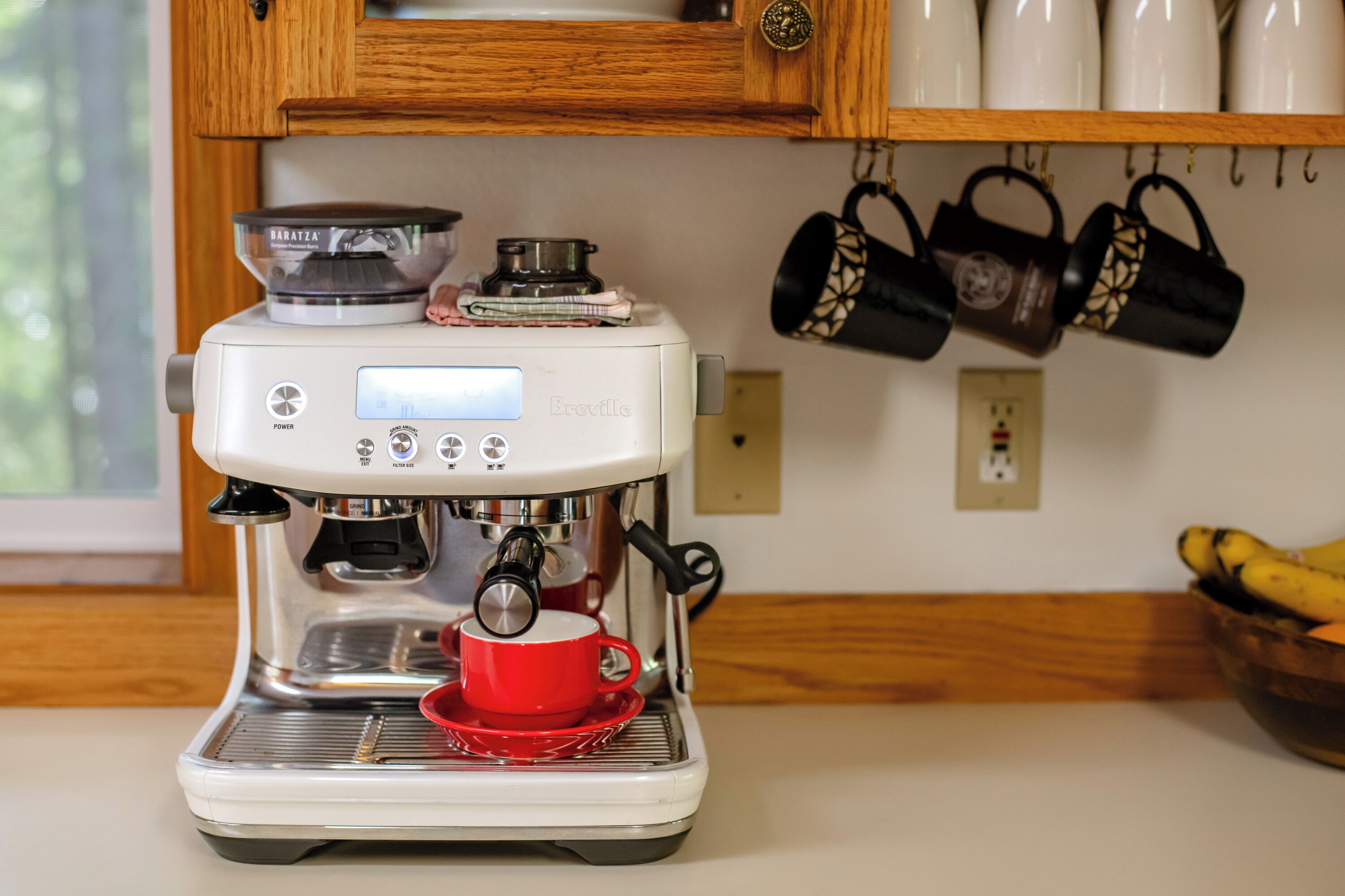 A coffee machine with a digital display, a red cup, and a kitchen counter.