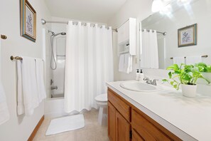 Un baño con ducha, inodoro, lavamanos y una planta en maceta.