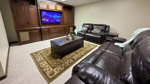 A living room with a large flat-screen TV, leather sofas, a coffee table, and wooden cabinets.