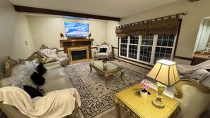 A living room with a fireplace, a television, and a large window with curtains.