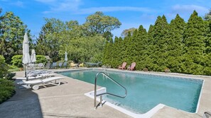 Ein rechteckiger Pool mit Metallleiter, umgeben von Liegestühlen und Sonnenschirmen.