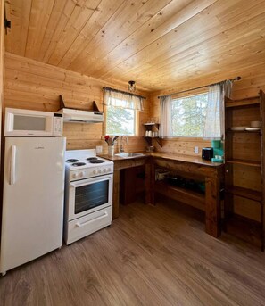 Una cocina compacta con paredes de madera, un refrigerador blanco, una estufa y un microondas.