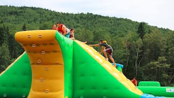 Eine aufblasbare Wasserrutsche mit mehreren Bahnen und einem bewaldeten Hügel im Hintergrund.