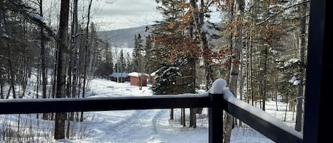 Paisaje nevado con una terraza de madera y vistas a un sendero cubierto de nieve que lleva a un edificio.