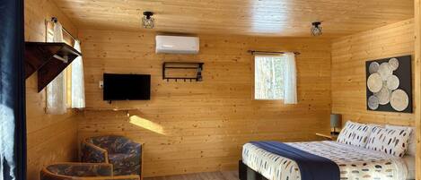 A wooden cabin room with a bed, a television, and a window.