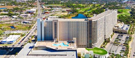 Un hotel moderno con piscina en la azotea y un campo de golf al fondo.