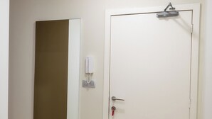 A room with a wooden floor, a white door with a key in the lock, a wall-mounted phone, and a table with plates and bowls. - Charming Studio | Downtown | 2min Metro | 401 (BRUXELLES)