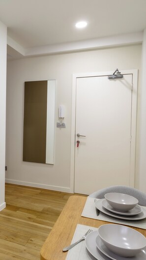 A room with a wooden floor, a white door with a key in the lock, a wall-mounted phone, and a table with plates and bowls. - Charming Studio | Downtown | 2min Metro | 401 (BRUXELLES)