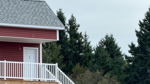 A two-story building with a red exterior and a white door. It features a wooden deck with white railings and a staircase leading to the upper floor. - Room-red Farm Inn - Room 12 (Howie Centre)