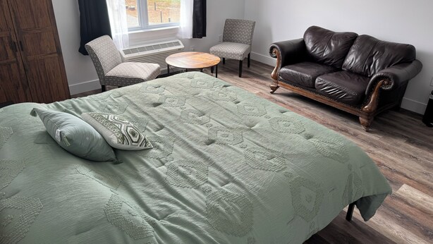 A bedroom with a large bed, a leather sofa, two armchairs, a small round table, and a window with curtains. - Room-red Farm Inn - Room 12 (Howie Centre)
