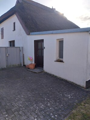 A single-story building with a dark roof, a small front porch, and a potted plant. - Small and quiet vacation apartment Helga (Glowe)