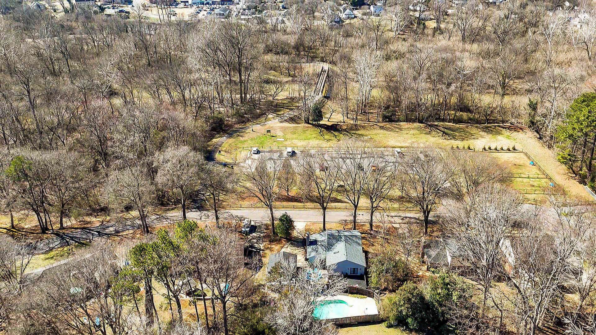 An aerial view of a residential area with a large open field, a swimming pool, and several houses.
