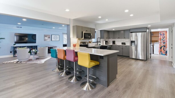 A modern kitchen with grey cabinets, stainless steel appliances, and a central island with colorful bar stools. - The GOAT - Pool, Hot Tub, Gym, Sauna & Gameroom (Belmont)