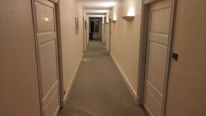 Een hotelgang met tapijttegels, crèmekleurige muren en deuren aan beide zijden.