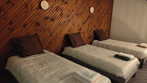 Twee eenpersoonsbedden met bruine kussens en witte lakens, houten wandbekleding en een ronde wandklok.