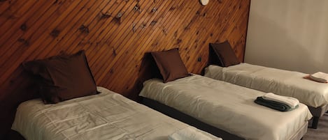 Two single beds with brown pillows and white linens, wooden paneling on the walls, and a round wall clock.