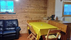 Interior acolhedor de madeira com uma mesa de jantar posta para quatro, um sofá de couro preto e uma área de cozinha com janela.
