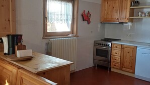 Une cuisine avec des meubles de rangement en bois, une cuisinière et une fenêtre ornée de rideaux en dentelle.