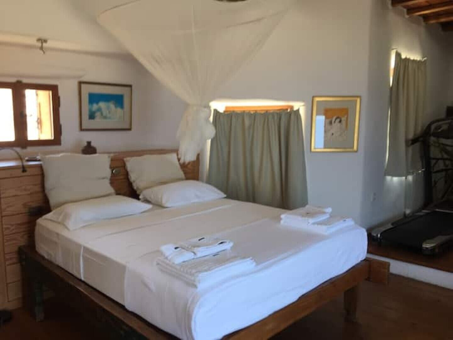 A neatly made bed with white linens, a wooden headboard, and a canopy. There are two pillows and a folded towel on the bed.