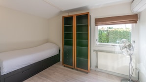 Et soveværelse med seng, skab, radiator og et vindue med udsigt til grønne omgivelser.