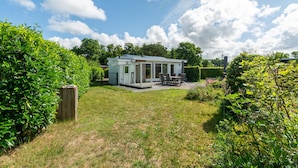 Et moderne hus med en patio, omgivet af frodigt grønt og en klar blå himmel.