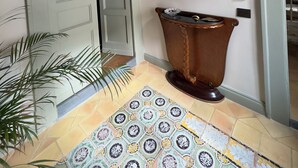 A hallway with a tiled floor, a large wooden urn, and several framed portraits on the wall. - Palazzo Carafa Santangelo - historic residence of the 400'in the heart of the ancient city (Napoli)