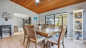 A dining area with a wooden table and chairs, a ceiling fan, and a glass cabinet with decorative items. - Spacious 3BR Heated Pool Home-Pets OK-12 min to beach (Cape Coral)
