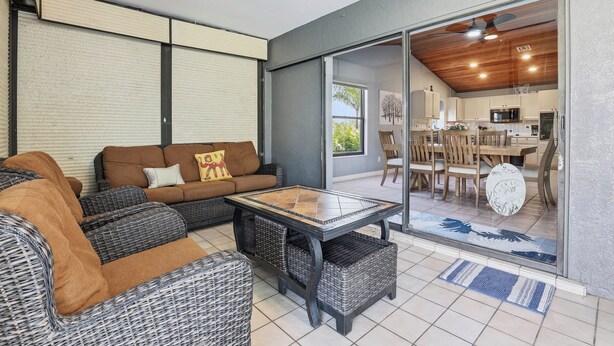 A modern living room with wicker furniture, a glass door leading to a kitchen, and a ceiling fan. - Spacious 3BR Heated Pool Home-Pets OK-12 min to beach (Cape Coral)